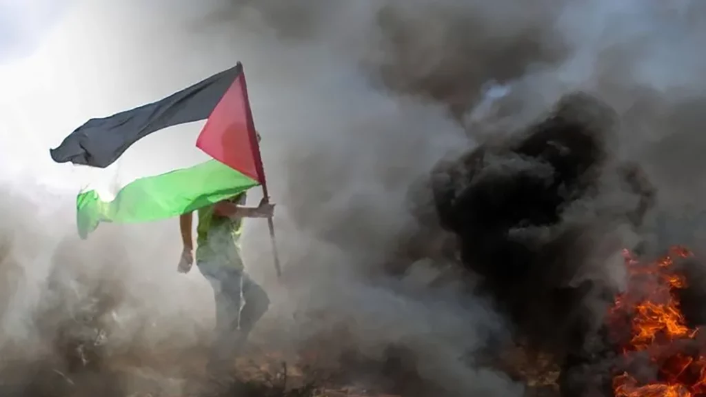 Maður gengur í gegnum reyk og eld með fána Palestínu í hendinni.